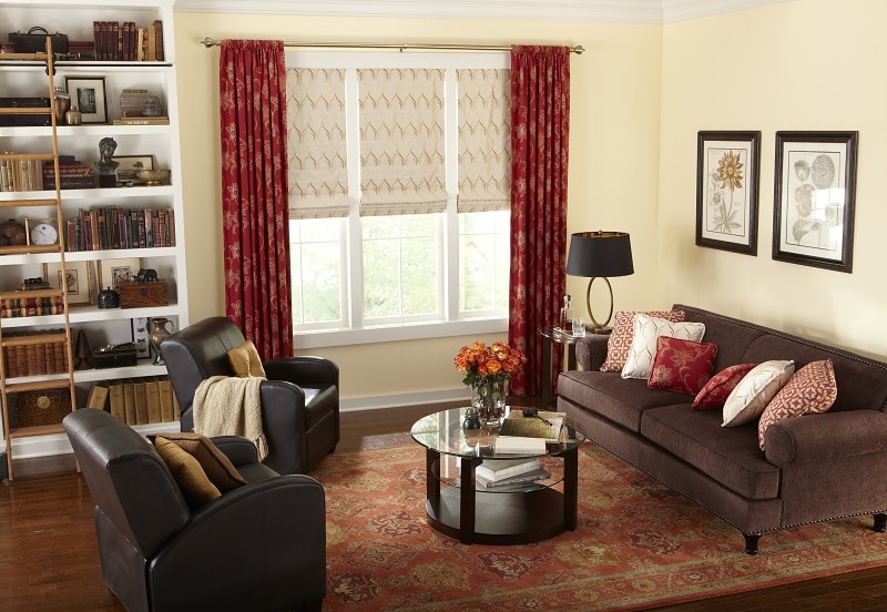 Layered roman shades paired with red drapery panels in a gorgeous living room.