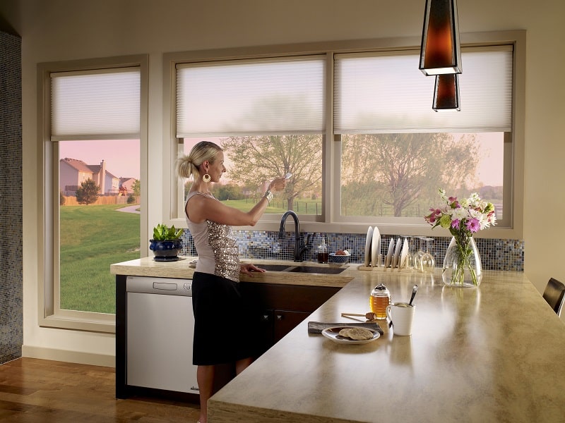 A woman controlling her motorized window treatments, one of the window fashion trends.