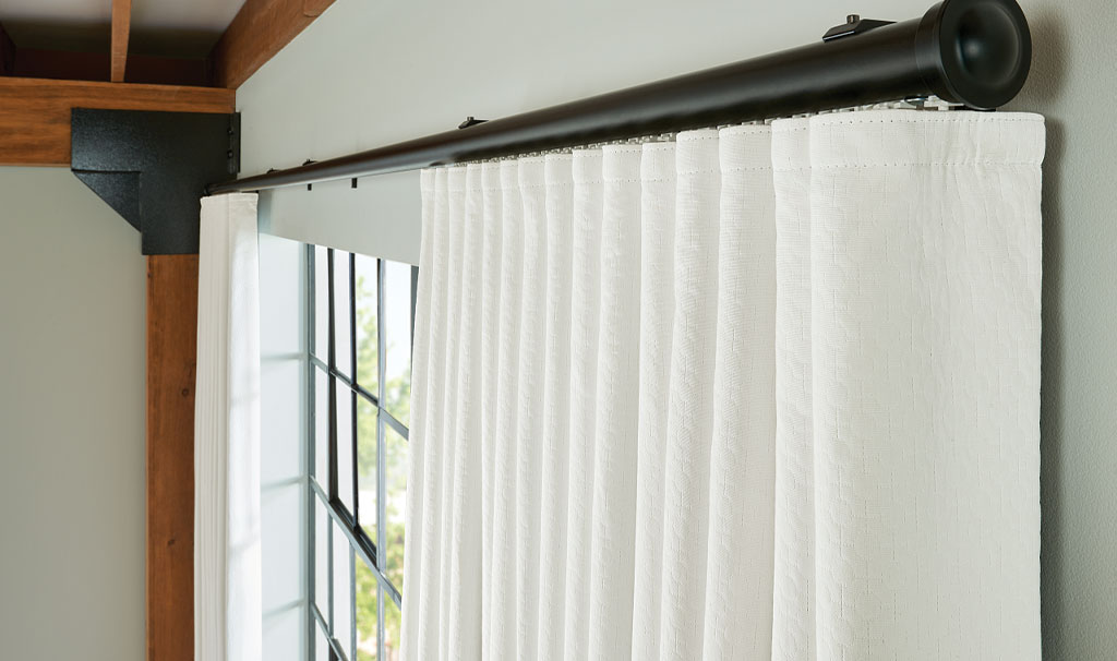 White blackout drapery panel on decorative black curtain rod in modern industrial-style room with wood beams and large grid windows
