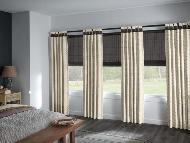 Bedroom with natural woven blackout shades layered behind patterned side panel drapery