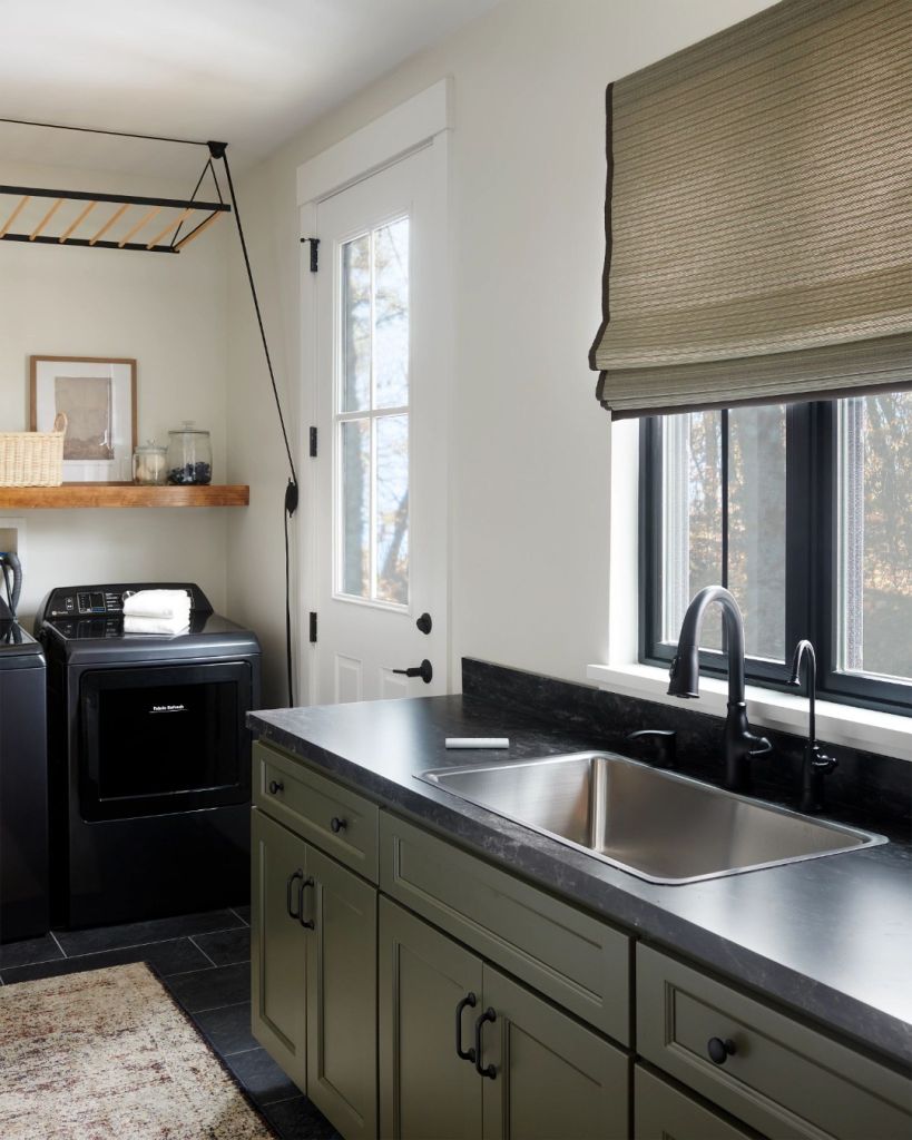 Laundry room with green cabinets, black counters, and Roman shade for a cozy fall look.